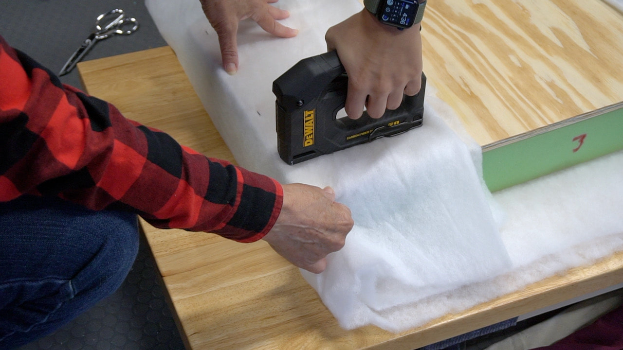 Using a DeWalt Carbon Fiber tacker to secure the batting to the plywood on the footstool.